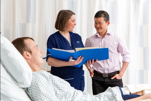 Two people standing with patient looking at book